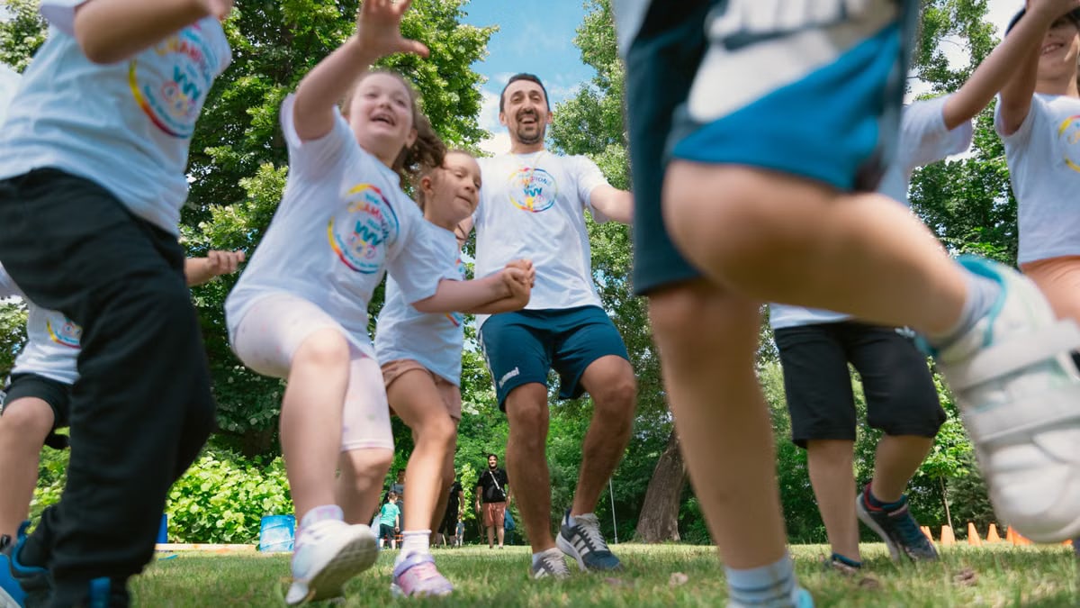 Joyful group of children and adult engaging in playful activities in a sunny park setting.